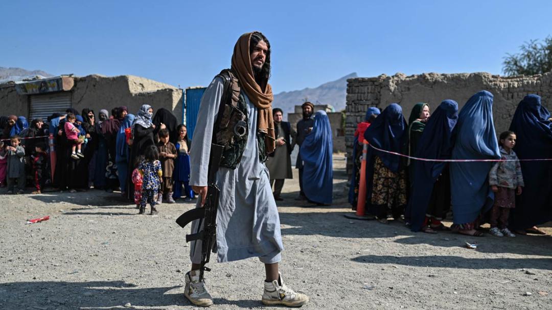 A Taliban fighter walks next to women waiting in line during a World Food Program food distribution on the outskirts of Kabul on November 6, 2021.